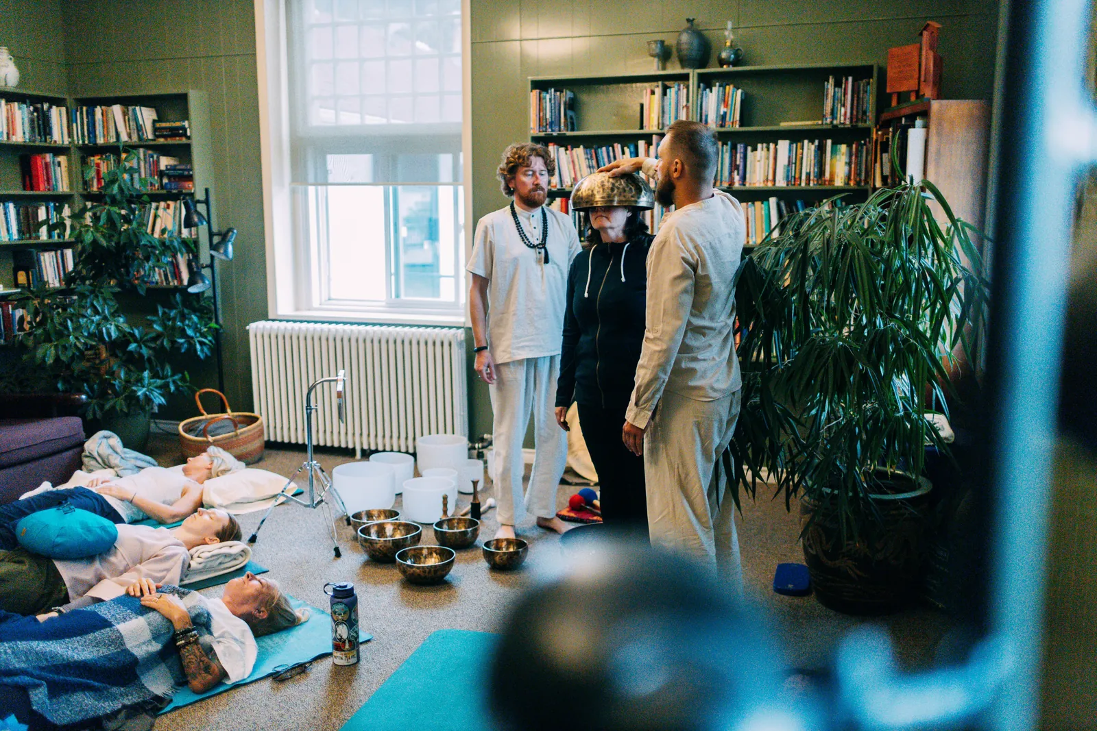 Group sound bath at Mount St. Francis: participants rest on mats while a teacher holds a singing bowl over a participant's head